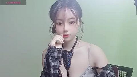 Media: A video of a young East Asian woman with fair skin, wearing a plaid shirt, dark hair, and a phone headset, against a plain green background.