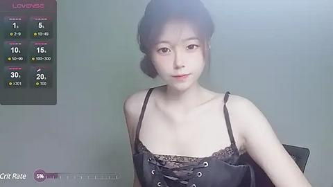 Media: Video of a young Asian woman with fair skin, black hair in a bun, wearing a black lace-trimmed top, against a plain gray background. A \"Love Meter\" display shows 70% compatibility.