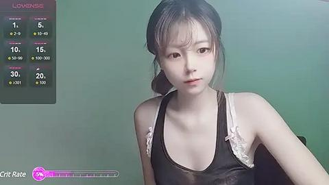 Media: A video of a young Asian woman with fair skin, wearing a black tank top with white lace, sitting against a plain green background. The image is taken from a video game, with a health bar and stats visible in the top left corner.