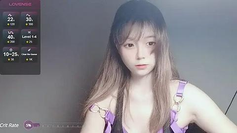 Media: Video of a young East Asian woman with long, straight brown hair, wearing a purple lingerie set, standing against a plain grey background.