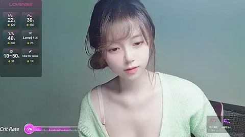 Media: Video of a young Asian woman with pale skin, dark hair, and a light green cardigan, sitting in a dimly lit room.