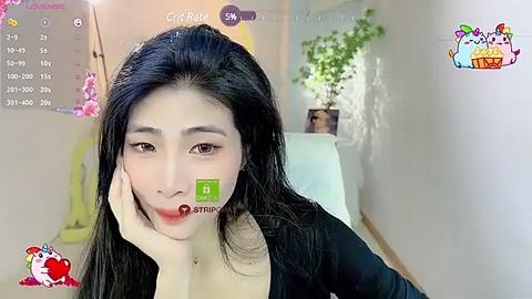 Media: A video of an Asian woman with long black hair, fair skin, and red lipstick, sitting on a white couch, looking into the camera. Background features a green plant and a colorful cartoon character.