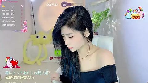 Media: Video of an Asian woman with long black hair, wearing a black off-shoulder top, sitting in a bright room with toys and plants.