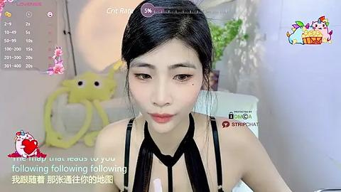 Media: Video of a young East Asian woman with smooth, fair skin, long black hair, and light makeup, wearing a black halter top, in a cozy, slightly blurred room with a calendar and cartoon figures.