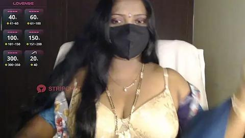 Media: Video of a South Asian woman with long black hair, wearing a black face mask, beige lace bra, floral kimono, sitting on a white chair.