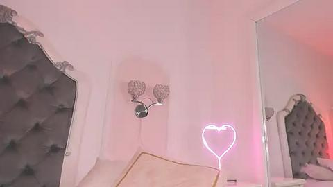 Media: Video of a pink-lit bedroom with a heart-shaped neon sign, tufted headboard, and a silver wall-mounted lamp.