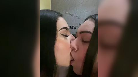 Media: Video of two women passionately kissing, one with long dark hair, the other with short dark hair, both with closed eyes. Background shows part of a wall with text.