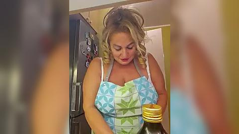 Media: Video of a blonde woman with curly hair, wearing a blue floral apron, focused on a jar of jam in a kitchen.