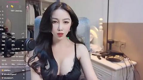 Media: Video of an East Asian woman with long black hair, wearing a black lace bra, sitting in a dimly lit room with a white desk, a camera, and a chair.