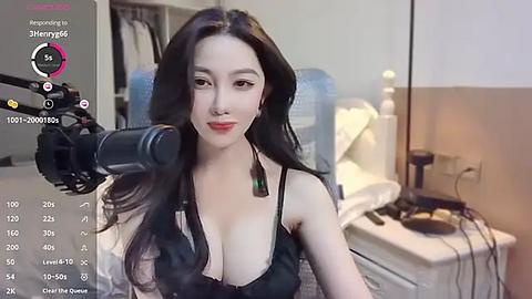 Media: Video of an Asian woman with long black hair, wearing a black lace bra, holding a microphone, in a bedroom with a bed and nightstand.