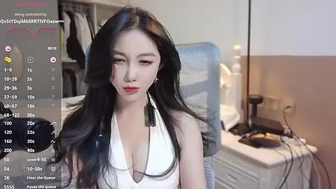 Media: A video of an Asian woman with long black hair and fair skin, wearing a white halter top, standing in a bedroom with a desk, computer, and clothes hanging in the background.