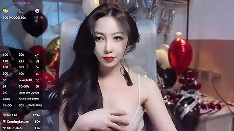 Media: Video of an Asian woman with long black hair, wearing a white dress, holding her breast, in a room with red and black balloons, and a table with a red lamp.