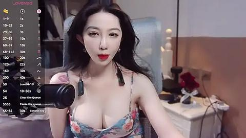 Media: A video of an East Asian woman with long black hair, wearing a revealing floral top, sitting in front of a webcam in a dimly lit room.