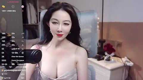 Media: Video of an East Asian woman with long black hair, wearing a low-cut white dress, recording herself with a black microphone in a modern bedroom with white furniture and a pink rose.