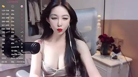 Media: Video of an East Asian woman with long black hair, red lipstick, and white top, recording herself on a phone in a bedroom with a bed, closet, and red roses.