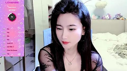 Media: Video of an Asian woman with long black hair, fair skin, and red lipstick, wearing a black lace top, sitting on a bed with white sheets, surrounded by plush toys.