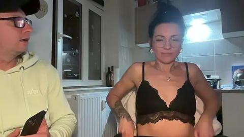 Media: A video of a middle-aged man with glasses and a cap, and a tattooed woman in a black lace bra, standing in a modern kitchen.