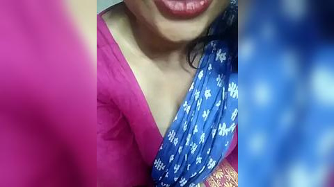 Media: Video of a woman in a vibrant pink blouse and a blue saree with white floral patterns, partially blurred. The focus is on her face, with lips slightly parted.