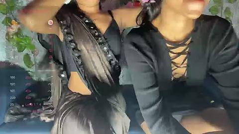 Media: Video of two women in black leather jackets, one with a gold lace top, sitting closely together on a blue sofa. Background includes a green plant.