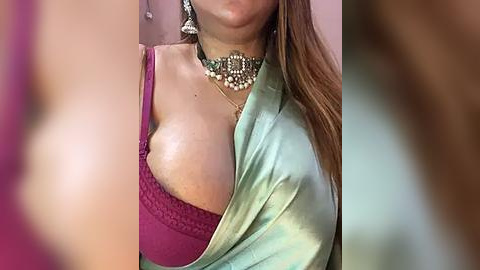 Media: Video of a woman with light skin, wearing a deep pink bra with lace details, draped in a light green silk robe, adorned with a golden necklace.