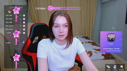 Media: Video of a young, fair-skinned, brown-haired woman in a white T-shirt, sitting in a red and black gaming chair in a dimly lit room.