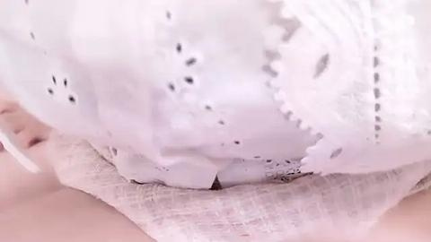 Media: A close-up video shows a white, lacy bra with delicate scalloped edges, partially obscured by a light, textured fabric. The image is focused on the bra's intricate design and the contrasting textures of the fabric.