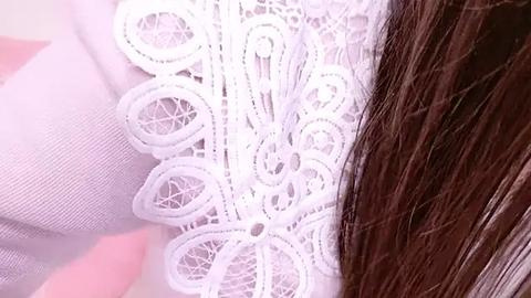 Media: Close-up video of a white lace garment with intricate floral patterns, partially covering long, straight brown hair. The fabric appears delicate and finely textured.