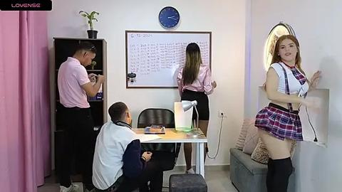 Media: Video of a classroom scene: A young Asian woman in a schoolgirl outfit stands provocatively by the wall, while a teacher and student work at a desk.