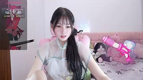 Media: A video of an Asian woman with long black hair, wearing a see-through blue top, sitting on a pink cushioned chair. A plush toy and a video game controller are visible in the background.