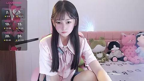 Media: Video of a young East Asian girl with long black hair, wearing a pink blouse, sitting on a bed with stuffed animals.