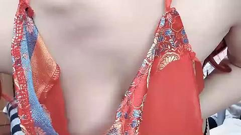 Media: A close-up video of a woman's chest in a coral lace bra with floral patterns. The bra straps are adorned with delicate pink and blue lace. The background is blurred, showing a hint of a white and blue striped shirt.