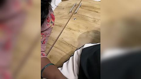 Media: A video captures a close-up of a woman in a pink floral dress and a man in a black and white shirt, sitting on a wooden floor, with a metal rod and tools nearby.