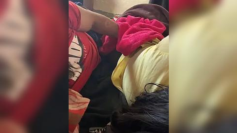 Media: A video shows a person sleeping on a bus, wearing a red shirt, with a pink blanket covering them, and another person in a yellow shirt visible in the background.