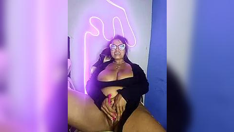 Media: Video of a plus-sized woman with large breasts, wearing a black crop top and open jacket, posing seductively in front of a glowing \"sun\" neon sign, with a blurred background.