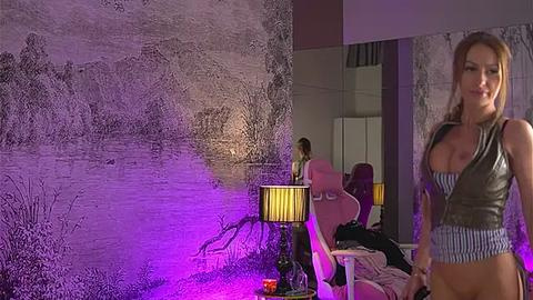 Media: Video of a woman in a low-cut, sleeveless top, standing in a dimly lit room with purple lighting, featuring a wall mural, lamp, and furniture.