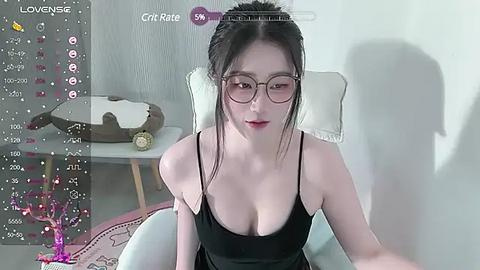 Media: A video of an Asian woman with glasses, red lipstick, and black hair, wearing a low-cut black dress, sitting in a modern chair. The room has a gray wall and a white table with a deer head.