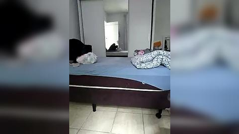 Media: A video of a messy bedroom with a bed covered in blue sheets, a black hat, white and pink clothes, and a partially open closet.