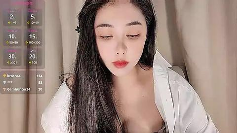 Media: Video of a young East Asian woman with long black hair, fair skin, and closed eyes, wearing an open white shirt, against beige curtains.