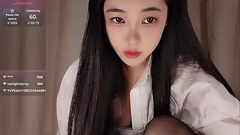 Media: Video of an Asian woman with long black hair, light skin, and full red lips, wearing a white blouse, indoors.