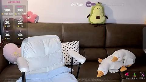 Media: A video depicts a brown leather couch with three plush toys: a pink bear, a green bean bag, and a white cat. The background shows a white wall with a \"Cry Rate\" display, indicating 100% at 19:00.