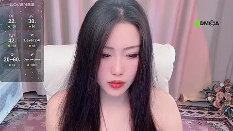 Media: Video of a fair-skinned Asian woman with long, straight black hair, wearing red lipstick, sitting on a bed with white sheets and a floral-patterned blanket, background shows curtains and a window.