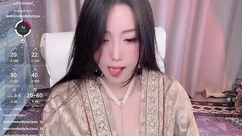 Media: Video of a young Asian woman with long black hair, wearing a gold satin robe, lying on a white cushion, with a live stream overlay.