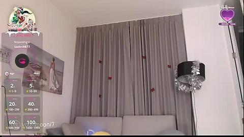 Media: A video of a modern living room with a grey sofa, grey curtains, and a silver spotlight. A TV screen displays a game interface. The room has a minimalist design with white walls.