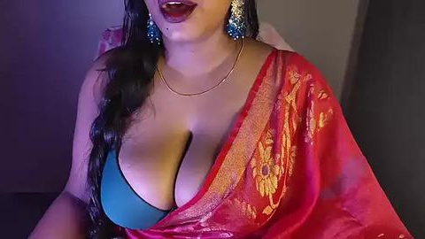 Media: Video of a South Asian woman with long black hair, wearing a red sari with gold embroidery, blue bra, and gold earrings.