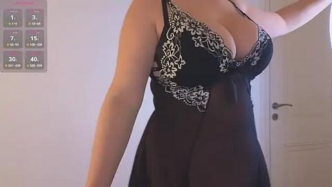 Media: Video of a light-skinned woman in a sheer black nightgown with intricate lace detailing on the chest, revealing ample cleavage. Background shows a white door and a digital clock displaying 15:19.