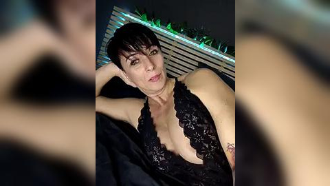 Media: Video of a slender, pale-skinned, short-haired woman in black lace lingerie, lying on a bed with a striped headboard and green fairy lights, looking seductive.