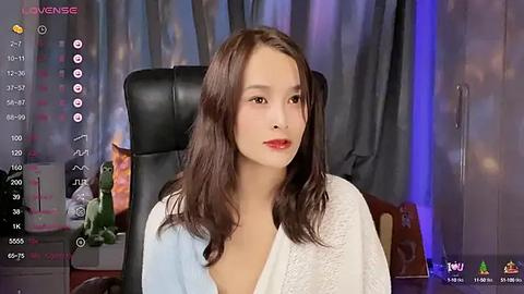 Media: A video of a young Asian woman with long, wavy brown hair, wearing a white robe, sitting in a black office chair. The background features a blurred, colorful, bokeh effect.