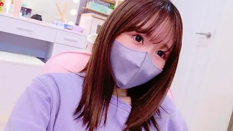 Media: Video of a young Asian woman with straight, shoulder-length brown hair, wearing a light purple lab coat and a light blue surgical mask. Background shows a white cabinet with various medical supplies.