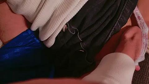 Media: Video of a close-up of two legs in casual clothing, including a white sock, dark shorts, and blue jeans, lying on a beige couch.