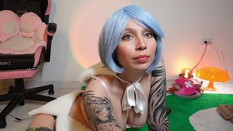 Media: Video of a pale-skinned woman with blue bobbed hair, wearing a black and white striped top, a septum ring, and a nose ring, sitting on a green rug, surrounded by a pink gaming chair, orange lamp, and a plush toy.